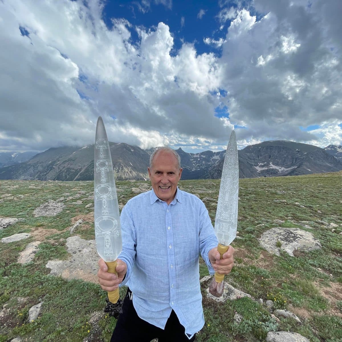 Tom Ledder holding two engraved Selenite Swords of Light against a mountain sky